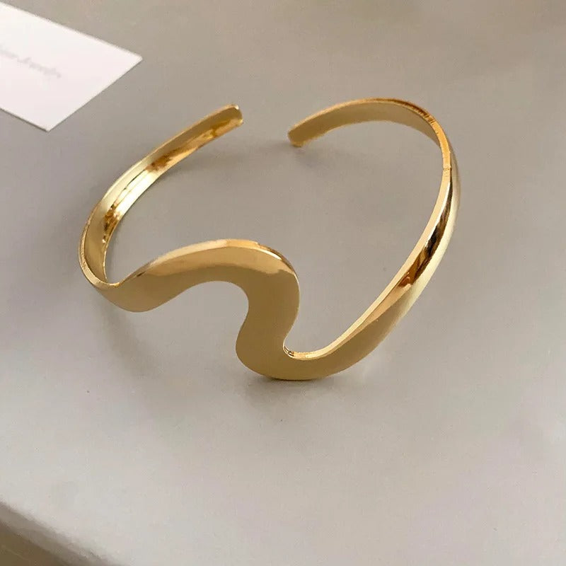 Elegant dame manchetarmbånd i guldlook med organisk skulpturel design. Et moderne og unikt statement smykke.