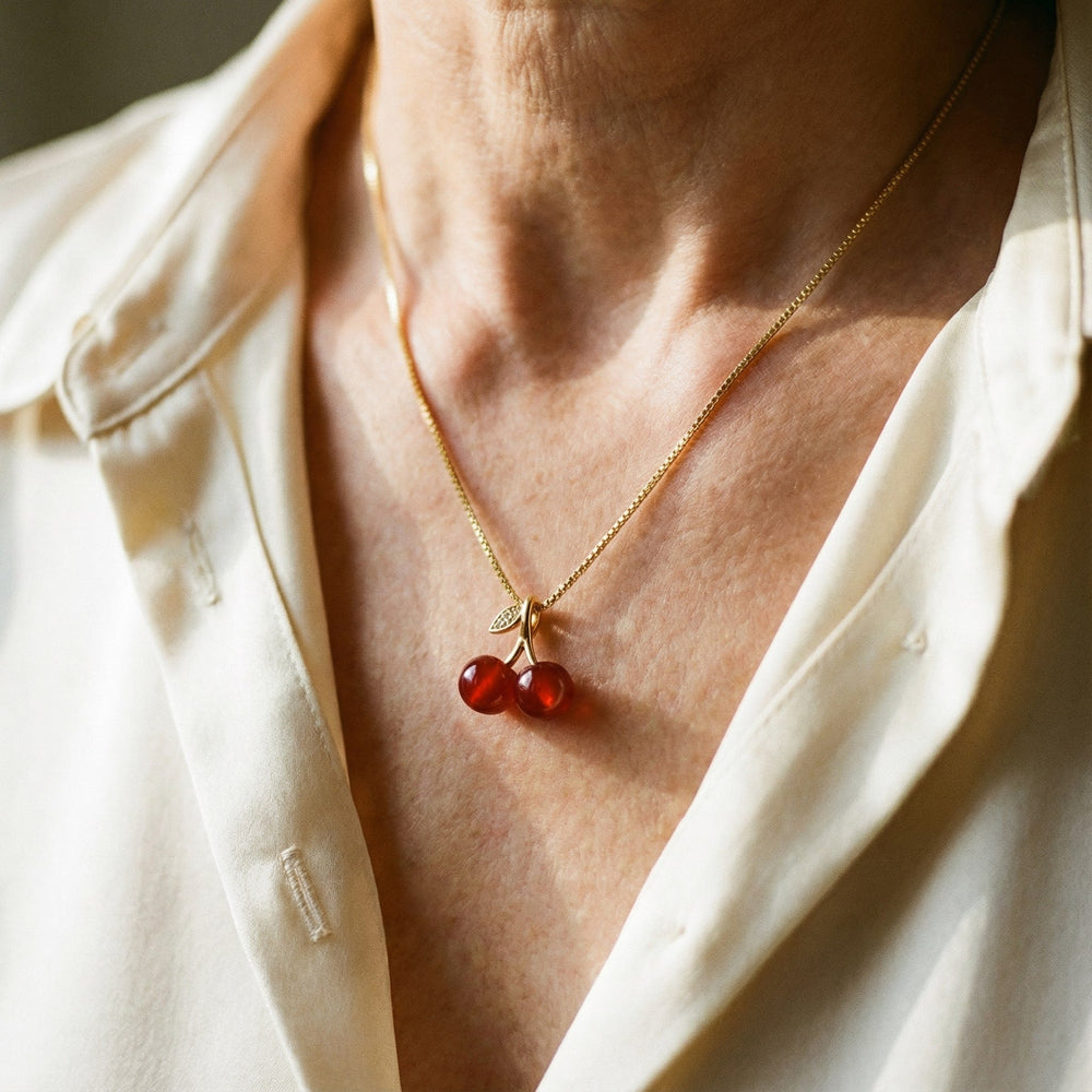 Feminint kirsebær halskæde i guld med rødt vedhæng. Stilfuldt damesmykke, ideel som moderne accessorie.