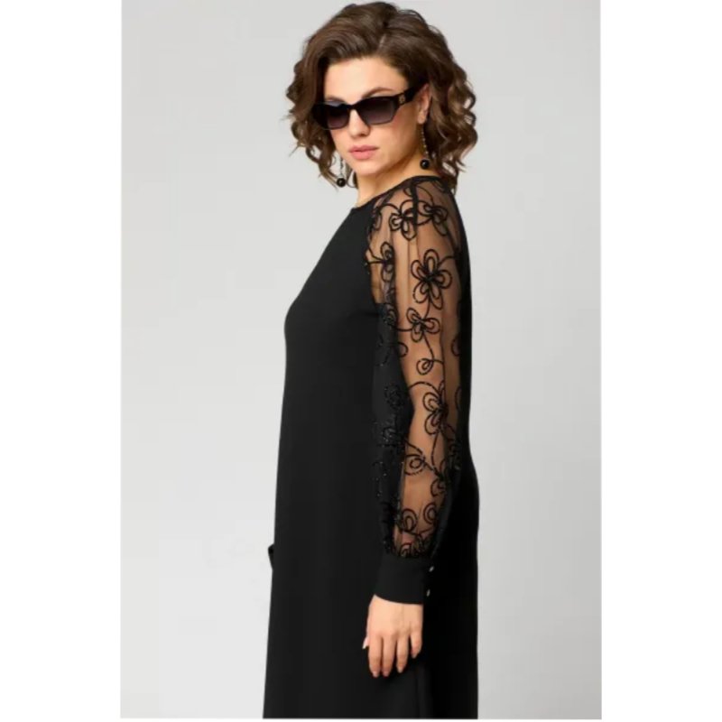 Model viser elegant plus size blondekjole i sort med transparente ærmer. Perfekt pasform til kurvede kvinder.