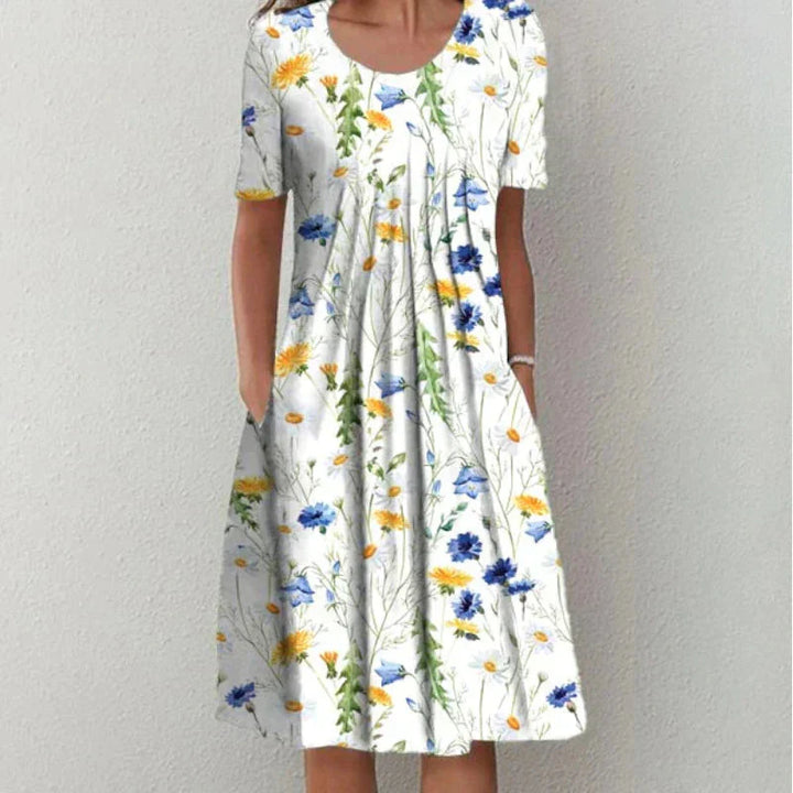 "Elegant Stilla Emma kjole i blå med blomster, flatterende silhuet, tidløst design til festlige lejligheder, fås i mange stør