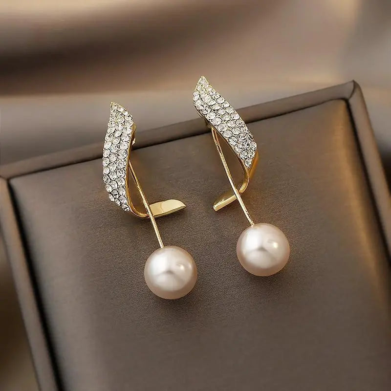 Elegante guldøreringe til kvinder med perle og funklende krystalvinge. Perfekte til fest og bryllup.