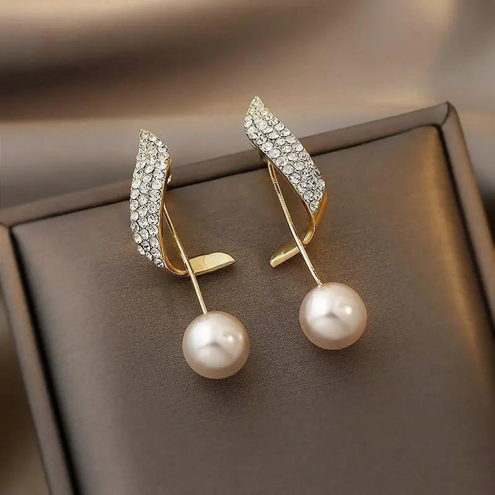 Elegante guldøreringe til kvinder med perle og funklende krystalvinge. Perfekte til fest og bryllup.
