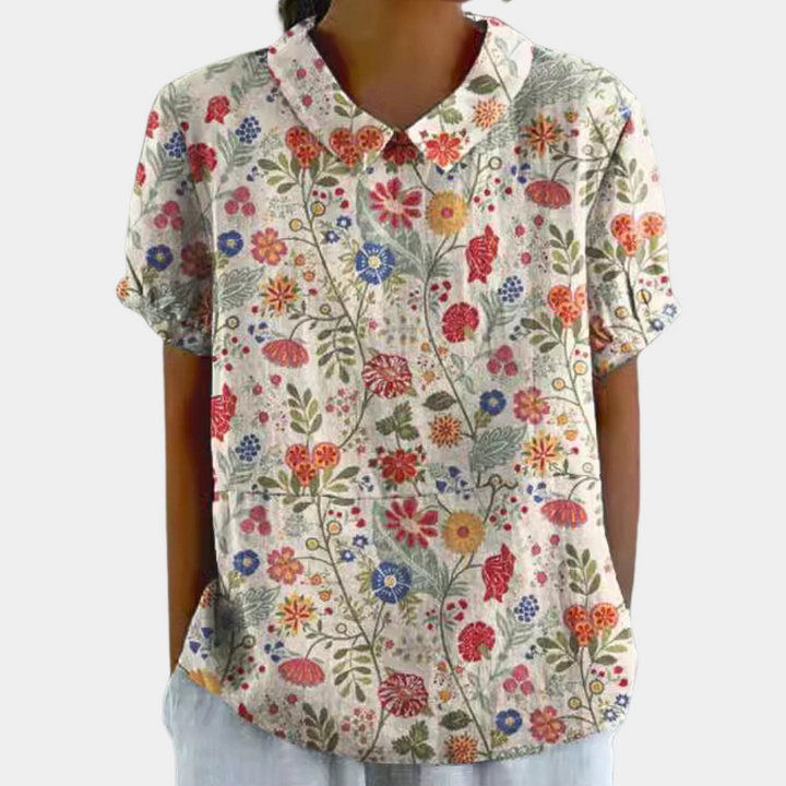 Farverig damebluse med smukt blomstermønster, korte ærmer og rund hals, perfekt til et stilfuldt hverdagslook.