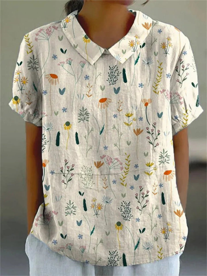 Hvid dame polo skjorte med elegant blomstermønster og løs pasform. Komfortabel casual top perfekt til sommeren.