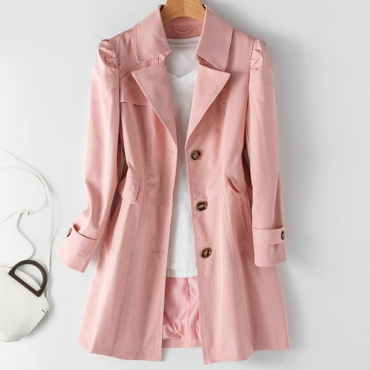 Kvindelig trenchcoat i beige med klassisk snit, knaplukning, letvægts og vandafvisende materiale. Set forfra mod baggrund.