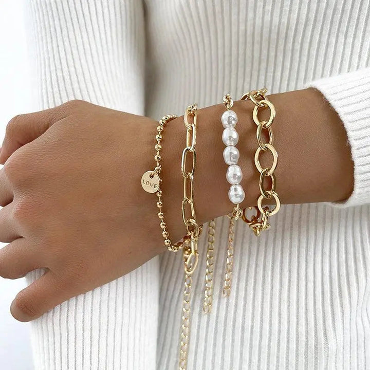 Lag-på-lag damearmbåndssæt i guld med elegante perler og kæder. Feminint smykke perfekt til enhver lejlighed.