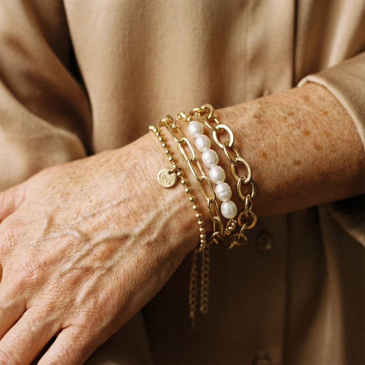 Guld armbåndssæt til damer med perle- og kædearmbånd i smukt lag-på-lag design. Elegant og feminint tilbehør.