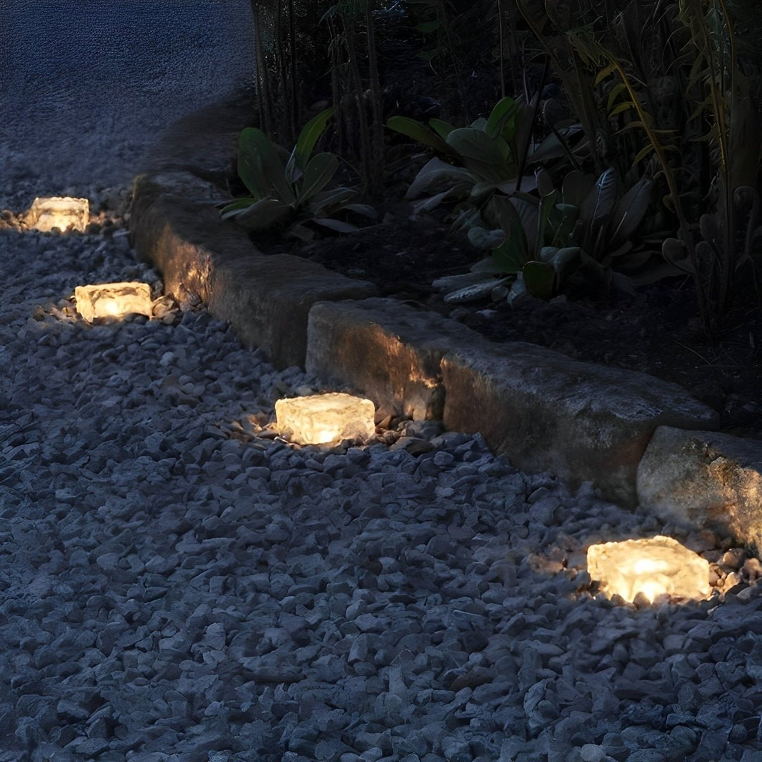 Terningformet solcellelampe placeret smukt i grøn have ved blomster.